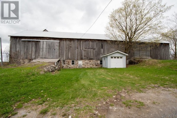 Long wooden barn with a stone foundation, grass, and a small grey shed. - 1444 5th Line, Selwyn