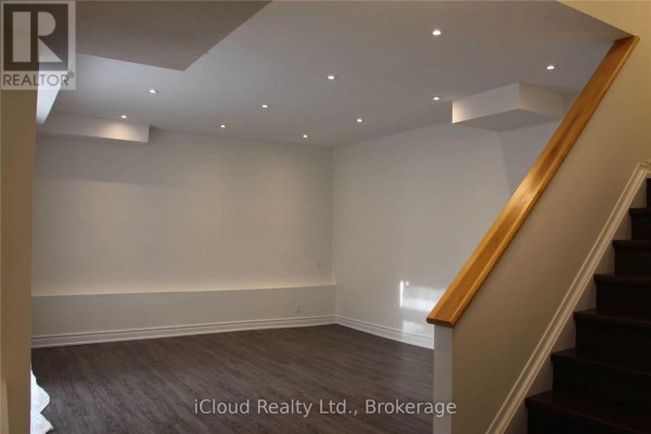 Empty room with dark laminate flooring, white walls, recessed lighting, and a built-in bench. - 1449 Ithaca Court, Mississauga