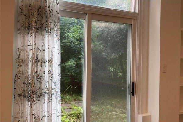 Sliding glass door with a floral sheer curtain on the left and a view of greenery outside. - 1449 Ithaca Court, Mississauga