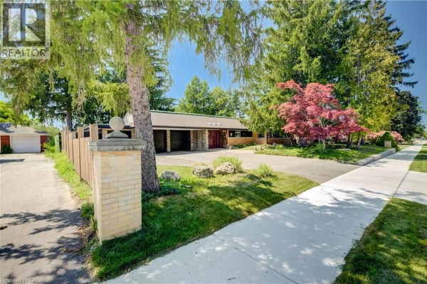 View of the property entrance with a brick pillar, fence, driveway, and mature trees. - 145 Ann Street, Kitchener