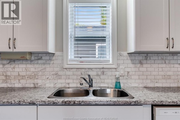 Close-up of a double stainless steel sink with a window above and marble tile backsplash. - 145 Dana, Essex