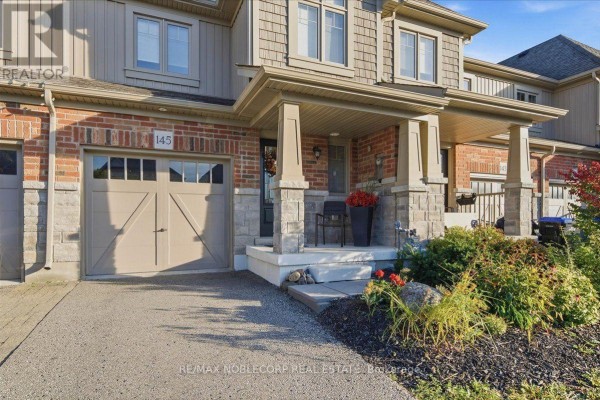 Close-up of a townhouse entrance with a garage door, porch, and stone accents. - 145 Hutchinson Drive, New Tecumseth