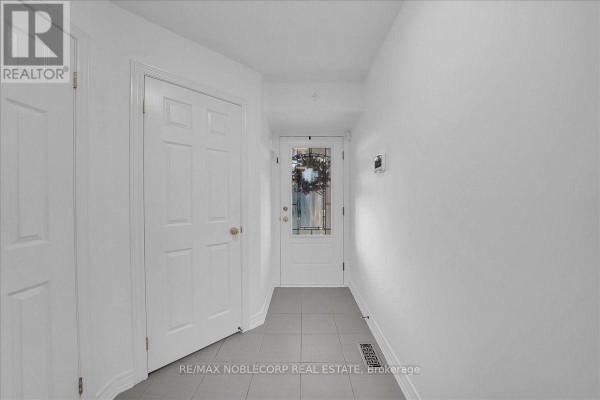 Interior view of a bright white hallway with tiled flooring and two closed doors. - 145 Hutchinson Drive, New Tecumseth