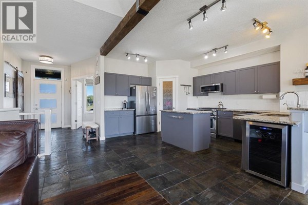 Modern kitchen with grey cabinets, stainless steel appliances, granite countertops, and a large island. - 145 Sharp Hill Drive, Rural Rocky View County