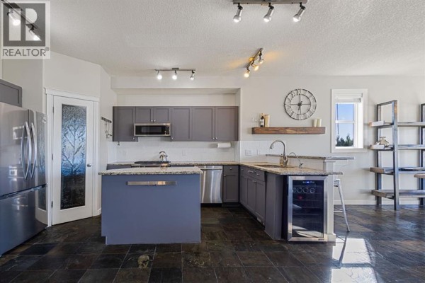 Spacious kitchen with grey cabinetry, a central island, stainless steel appliances, and dark slate flooring. - 145 Sharp Hill Drive, Rural Rocky View County