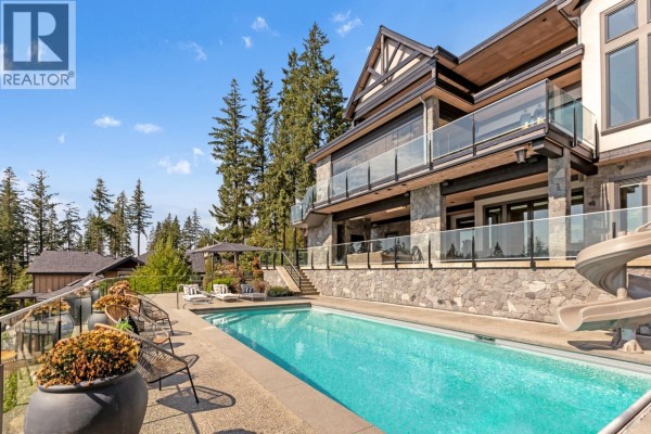 Rear exterior of a luxury home with a swimming pool, slide, patio furniture, and forest views. - 1450 Crystal Creek Drive, Anmore