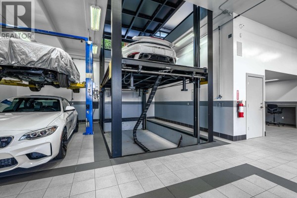Interior of a spacious garage with a car lift, two cars, and a workbench area. - 1450 Crystal Creek Drive, Anmore