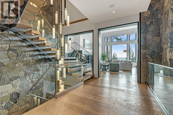 Foyer of a luxury home with a floating staircase, stone accent walls, and a view to the living room. - 1450 Crystal Creek Drive, Anmore