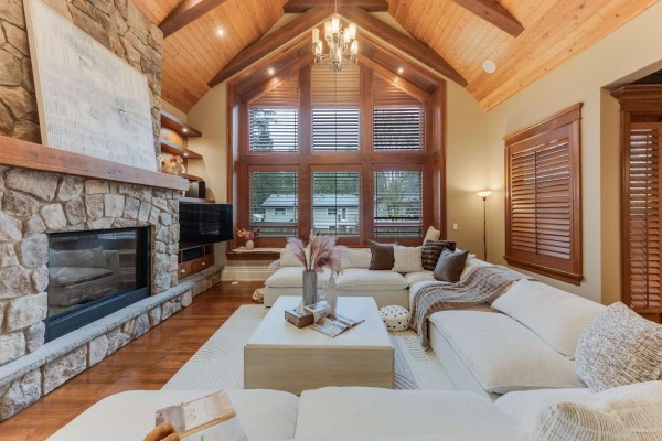 Living room with stone fireplace, built-in shelves, wood ceiling, and curved staircase. - 14526 32b Avenue, Surrey