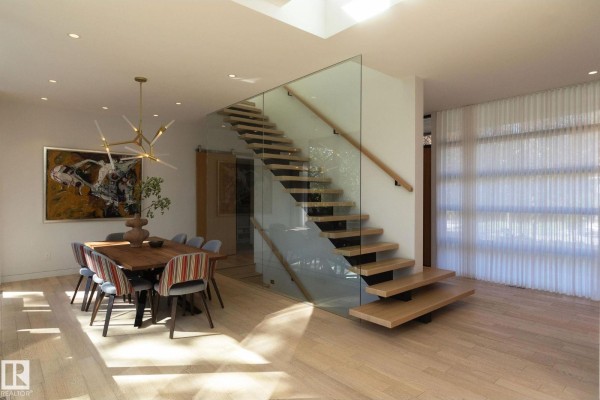 Dining area with a wooden table, colorful chairs, and a contemporary chandelier next to a glass-railed staircase. - 14530 Ravine Dr Nw, Edmonton