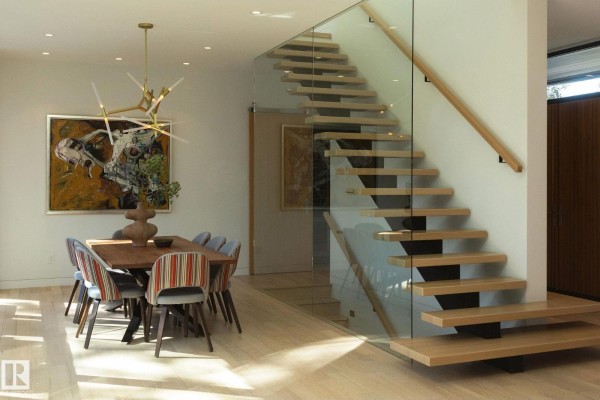 Open-concept living space with a dining table, chairs, and a floating wood staircase with glass railings. - 14530 Ravine Dr Nw, Edmonton