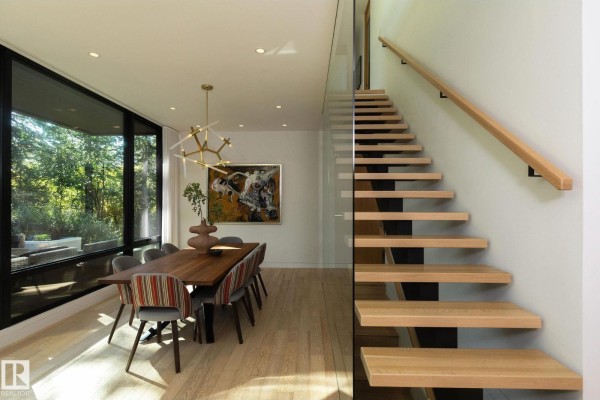 Dining room with a large window overlooking trees, a wooden table set for eight, and a unique modern chandelier. - 14530 Ravine Dr Nw, Edmonton