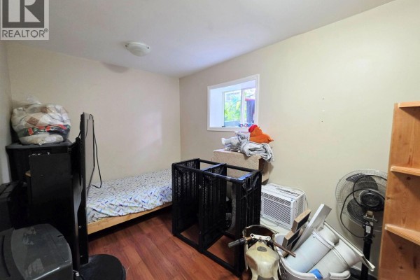 Small bedroom with a twin bed, hardwood floors, and storage shelves. - 1456-1462 Milburn Avenue, Prince George