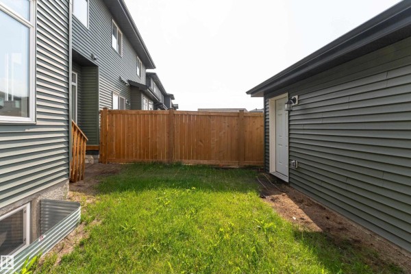 Backyard corner with a wooden fence, green grass, and the side of a detached garage. - 1457 Keswick Dr Sw, Edmonton
