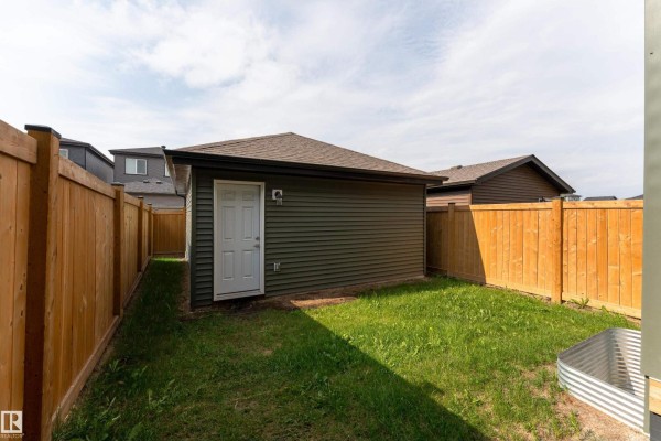 View of a detached garage in a fenced backyard with green grass and wood fencing. - 1457 Keswick Dr Sw, Edmonton
