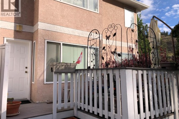 Close-up view of townhouse unit 119 entrance with white railing and potted plants. - 1458 Penticton Avenue Unit# 119, Penticton