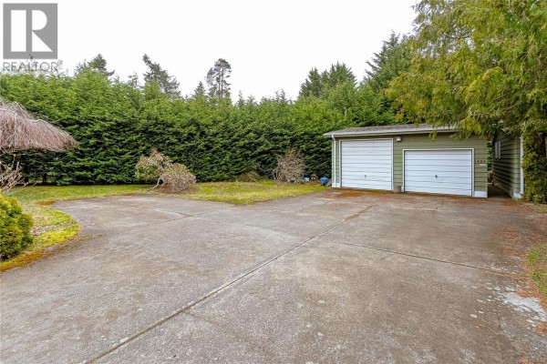 Concrete driveway leading to garage, bordered by hedges and lawn. - 1459 Sunrise Dr, Parksville