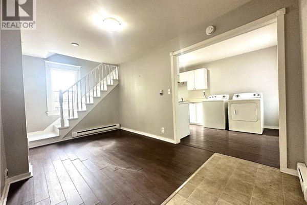 Living room with dark wood floors and a staircase, looking into the kitchen area. - 146 Dominion Street, Moncton