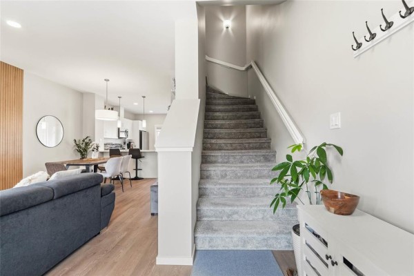 Interior view showing a gray carpeted staircase, gray sofa, dining area, and kitchen island. - 146 Emberwell Street, Winnipeg