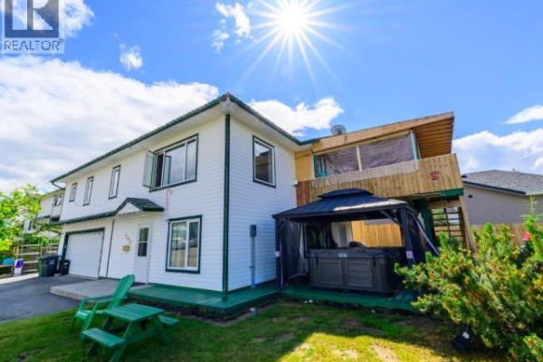 Rear exterior view of the house with a covered hot tub, deck, and lawn. - 146 Falcon Drive, Whitehorse