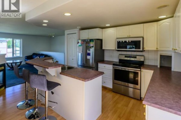 Kitchen with white cabinets, stainless steel appliances, and a breakfast bar with stools. - 146 Falcon Drive, Whitehorse
