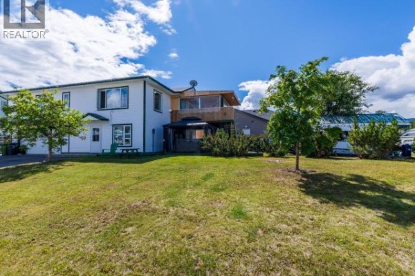 Backyard view of the white house with a large grassy area and mature trees. - 146 Falcon Drive, Whitehorse