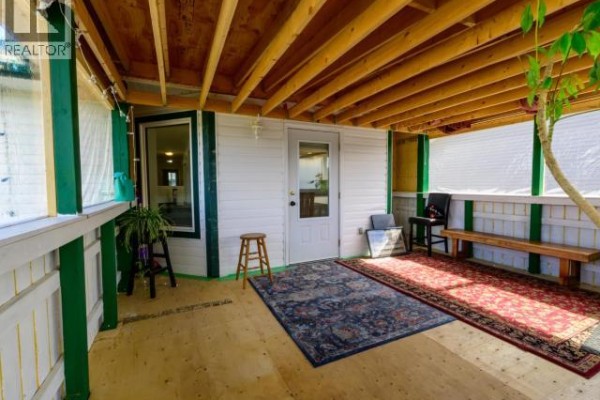 Covered patio with wooden beams, rugs, seating, and a door leading inside. - 146 Falcon Drive, Whitehorse