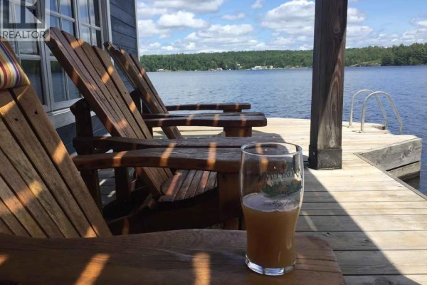 Wooden Adirondack chairs on a dock overlooking a lake with a glass of beer. - 146 Maplehurst Road, Seguin