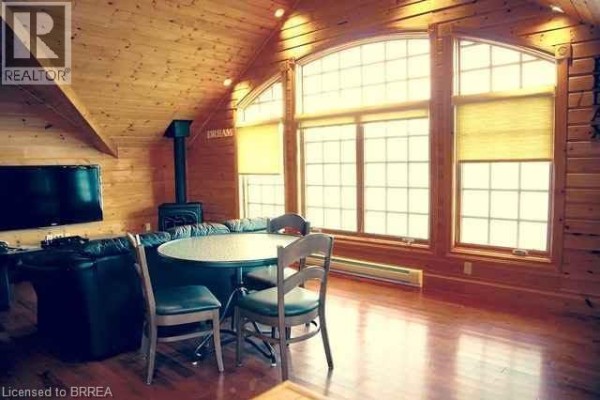 Living area with wood-paneled walls, a wood stove, and large arched windows with lake view. - 146 Maplehurst Road, Seguin