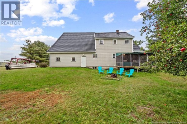 Rear exterior of a light grey house with a screened-in porch and teal chairs on a large green lawn. - 1460 Saint Charles Nord, Saint Charles