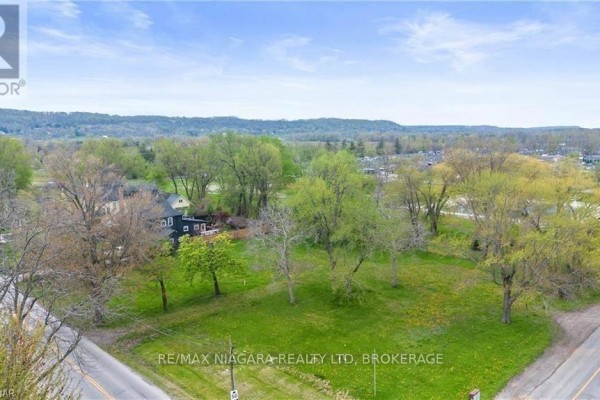 View of a spacious green lot with scattered trees and nearby residential properties. - 14662 Niagara River Parkway, Niagara On The Lake