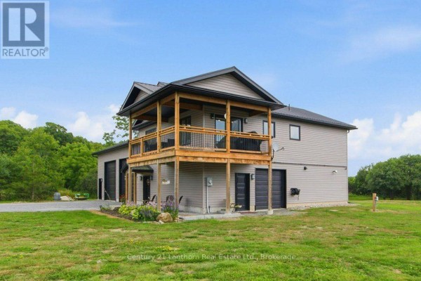 Side view of a grey house with a covered upper deck and attached garage doors. - 1467 County Road 19, Prince Edward County