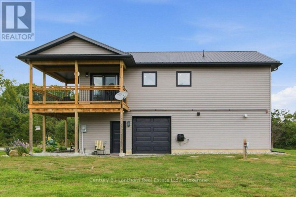 Rear side of the grey house featuring a large deck and multiple garage doors. - 1467 County Road 19, Prince Edward County