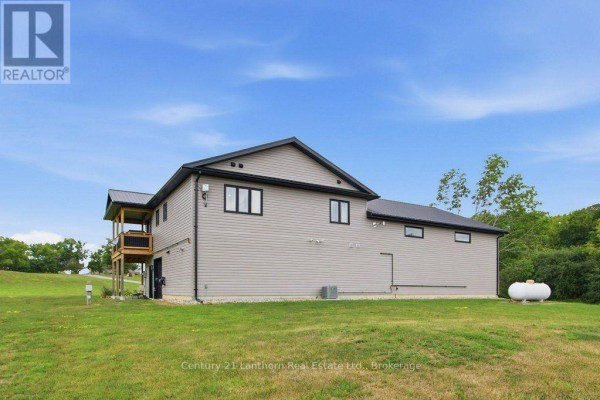 Far side view of the grey house with a metal roof and propane tank on the lawn. - 1467 County Road 19, Prince Edward County