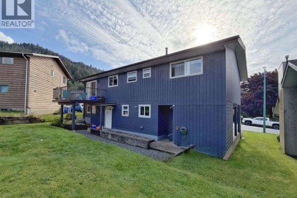 Rear view of the dark grey house with a balcony on the upper level and grass lawn. - 147-149 Gull Crescent, Prince Rupert