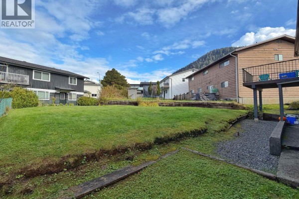 Expansive backyard with green grass, tiered garden beds, and adjacent houses. - 147-149 Gull Crescent, Prince Rupert