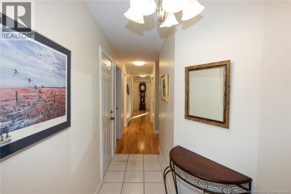 Hallway with hardwood floors, multiple doors, and a grandfather clock at the end. - 147 Arbour Brook Lane, Fredericton