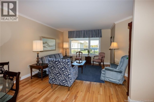 Living room with hardwood floors, blue patterned chairs, and a striped sofa. - 147 Arbour Brook Lane, Fredericton