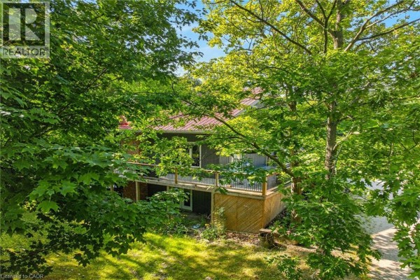 Rear exterior of a home with a dark grey siding, red metal roof, and a large wooden deck. - 147 Concession 1 Road S, Cayuga