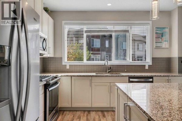 Kitchen sink area with a window overlooking townhouses, tiled backsplash, and granite countertops. - 147 Copperstone Park Se, Calgary