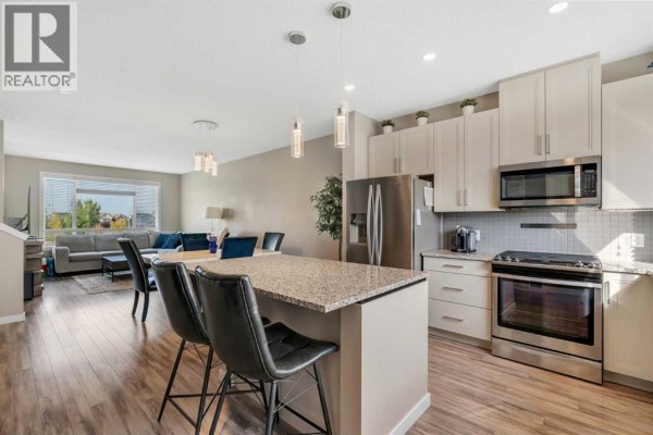 Open-concept kitchen and living area with a kitchen island, dining table, and living room furniture. - 147 Copperstone Park Se, Calgary