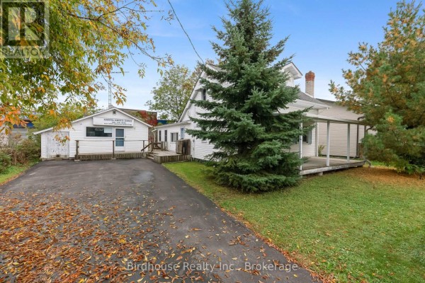 Side view of a white vinyl-sided house with a covered porch and a detached white building with windows. - 147 East Street N, Kawartha Lakes