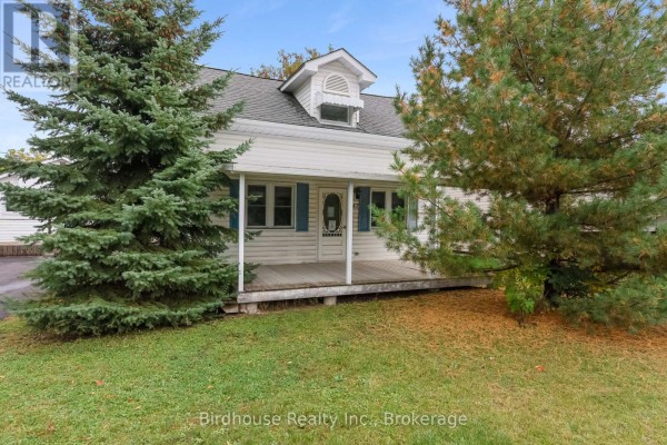 Front view of a white house with a small covered porch, blue shutters, and green lawn with trees. - 147 East Street N, Kawartha Lakes