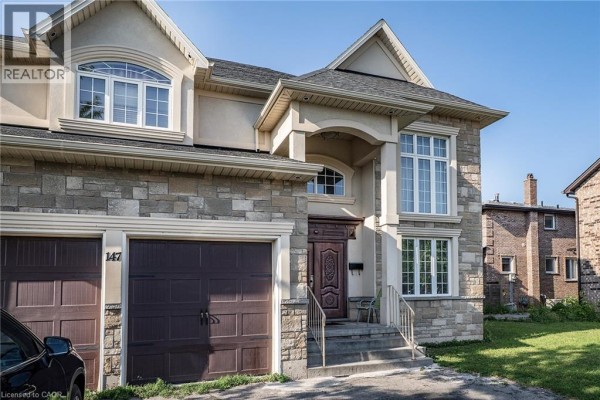 Close-up of the front entrance and garage doors of a stone and stucco house with arched windows. - 147 Federal Street, Stoney Creek