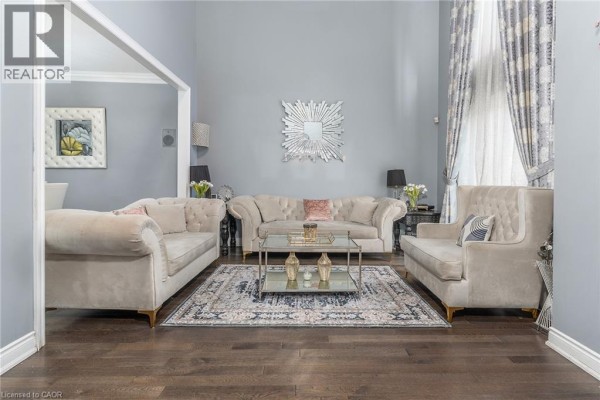 Living room with beige tufted sofas, a glass coffee table, and dark wood floors. - 147 Federal Street, Stoney Creek