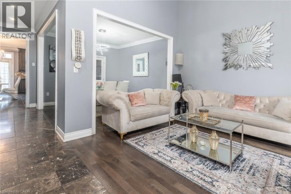 Living room featuring beige tufted sofas, a glass coffee table, and a patterned area rug. - 147 Federal Street, Stoney Creek