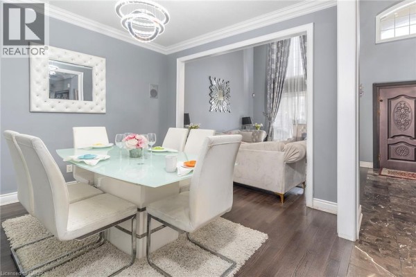 Dining room with a white glass-top table, white chairs, and a view into the living room. - 147 Federal Street, Stoney Creek