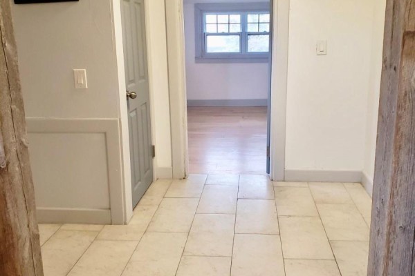 Hallway with light beige tiled floor, gray door, and doorway to a bright room. - 147 Holton Avenue S, Hamilton