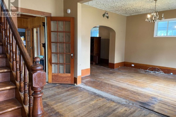 Interior view of a room with hardwood floors, a staircase, double doors, and an arched doorway. - 147 Mackay Street, Stellarton