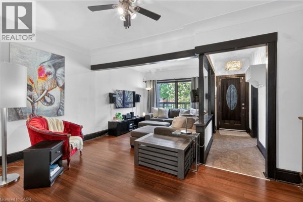 Living room with hardwood floors, a red armchair, and an opening to the entryway. - 147 Strachan Street E, Hamilton